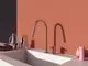 Küchenarmatur in glänzendem Roségold an einem modernen weißen Waschbecken. Im Hintergrund eine orangefarbene Wand. Produkte von Ideal Standard sind sichtbar.